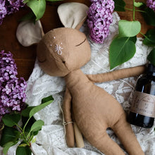 Charger l'image dans la galerie, Handmade brown linen mouse spirit guardian doll with embroidered facial features and a delicate symbol on its forehead, displayed on a wood and lace backdrop, surrounded by fresh lilac blossoms