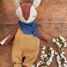 Charger l'image dans la galerie, Handmade linen fox spirit guardian doll wearing mustard overalls and a blue scarf, featuring a hand-embroidered rune-like symbol on its forehead, displayed with a sprig of black locust flowers against a natural wood backdrop